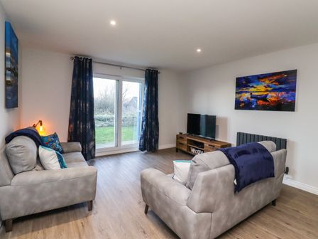 A living room with two grey sofas a wooden TV stand with a TV and blue curtains at 2A The Anchorage in Beadnell