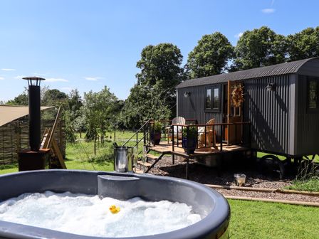 An outdoor hot tub with bubbles and a rubber duck next to a small cabin with a wooden porch and chairs at Herdwick Luxury Glamping in Nottingham
