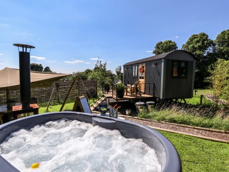 An outdoor area with a bubbling hot tub a small elevated cabin and lawn at Southdown Luxury Glamping in Nottingham