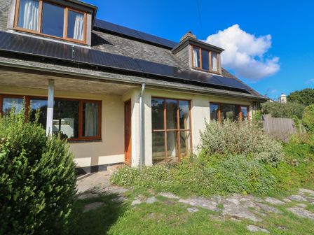 A cream house with wooden windows and solar panels on roof surrounded by greenery at Mulberry Cottage in Staple near Dartington