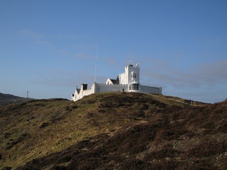 A white castle-like building on a hill with antennas and clear sky at East Point Lynas Lighthouse Keeper's Cottage in Llaneilian near Amlwch
