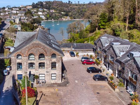 A cobblestone parking area with parked cars between stone buildings near a water body at 4 The Pottery in Dartmouth