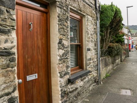Stone building with wooden door and window beside a sidewalk with green bushes and street lamp at Jessie's Cottage in Staveley