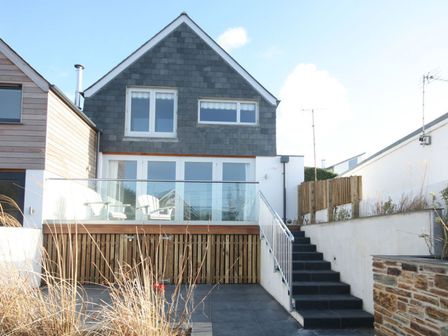 An exterior view of a two-story house with a balcony and outdoor chairs at The Beach House in Polzeath