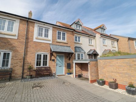 A row of brick and stucco terraced houses with benches and potted plants at Brucap Cottage in Beadnell