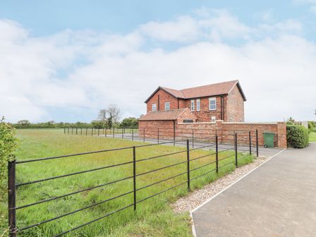 A brick house with a tiled roof next to a grassy field and a metal fence at Foremans Cottage in Withernsea