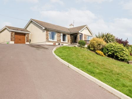 A single-story house with a tiled roof a garage on the left and shrubbery on the right at An Radharc Alainn Maul near Rosscarbery County Cork