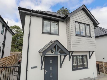 Front view of a two-story house with a dark door and windows a rowing roof and a fence at Iscoed in Llangefni