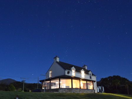 A lit two-story house with large windows under a starry night sky at Casey House in Filane Middle near Castletownbere County Cork
