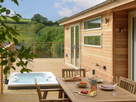 A wooden outdoor deck with a hot tub and a dining table set with food and drinks at 4 Valley View in Lanreath