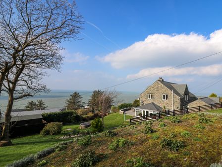A stone house with a garden and trees overlooking the sea at Mynydd ar Mor in Barmouth
