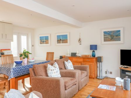 A living room with brown armchairs a wooden dining table with blue tablecloth and framed pictures on the wall at 3 Bonaventure Close in Salcombe