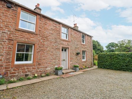 A stone house with four windows a door and flower pots in front at Garden Cottage in Great Salkeld