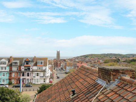 View of rooftops and a street with cars leading to a church tower and hills in the background at Flat 3 in Cromer