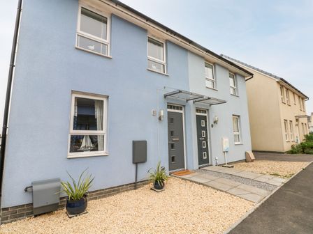 A two-door modern house with blue exterior walls and small front yards with potted plants at Ty Glas in Ogmore-by-Sea near St Brides Major