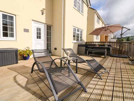 A wooden deck with two lounge chairs a small table a potted plant a seating area with a bench and umbrella at Sunny Views in Combe Martin