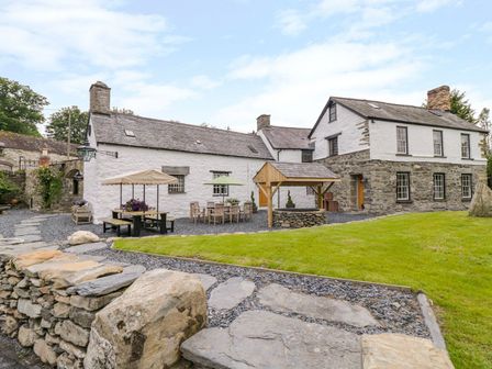 A stone and white plaster house with outdoor seating and a wooden well in a garden at The Druids in Druid near Corwen
