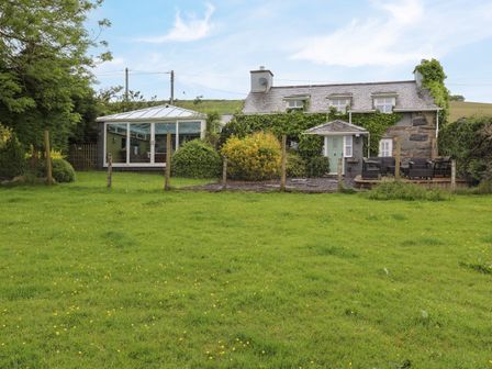 A stone house with ivy on the walls a conservatory and a fenced garden at Ty Newydd in Llanaelhaearn