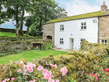A stone cottage with a mossy roof and garden with pink flowers and stone walls at The LA'AL Cragg in Kirkby Stephen