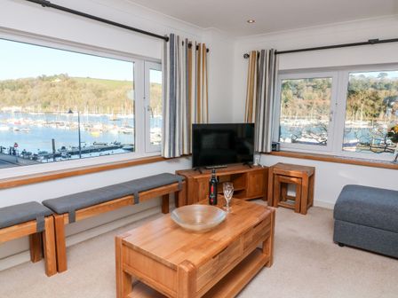 A living room with wooden furniture and a television overlooking a marina at Leeward in Dartmouth