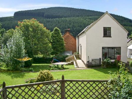 A garden with trees table and chairs in front of a white house at Tailors Cottage in Abbeycwmhir near Rhayader