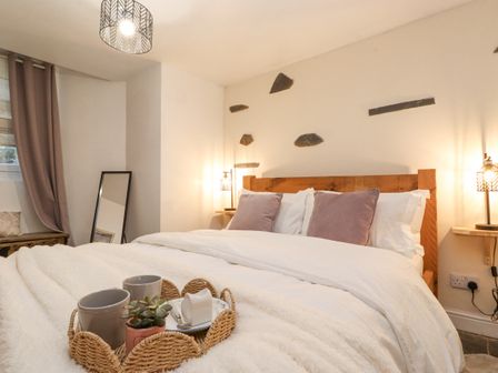 A bedroom with a wooden bed, white bedding, cushions, bedside lamps, a small mirror, and a tray with cups and a plant at The Wonky Burrow in Bowness-On-Windermere