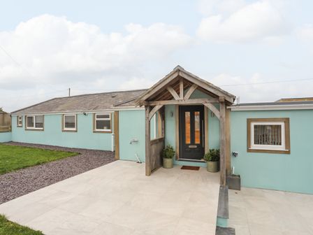 The exterior of a single story house with a blue facade a black front door wooden porch and a tiled patio at Bryn Llwyd Cottage in Burwen near Amlwch