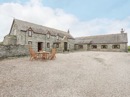 A stone house with multiple windows and a gravel courtyard with wooden table and chairs at Caerdegog Ganol in Cemlyn near Cemaes Bay
