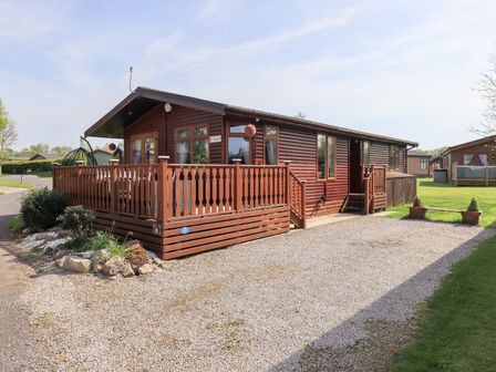 A wooden cabin with a fenced porch and gravel driveway at Our Happy Place Lakeside 16 Borwick near Carnforth