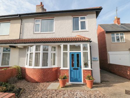 The front exterior of a two-story house with a blue door bay window and two flower pots at North Bay Cottage in Bridlington