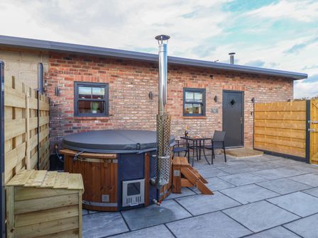 An outdoor patio area with a hot tub a small table with two chairs and a brick building at Robins Nest in Pocklington