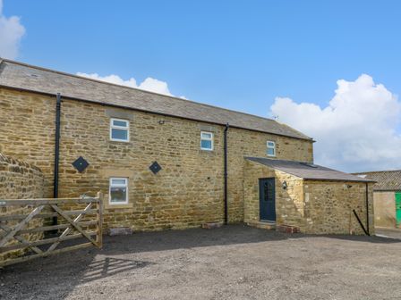 An outdoor view of a stone building with a wooden gate and a black door at The Coach House in Great Whittington near Corbridge