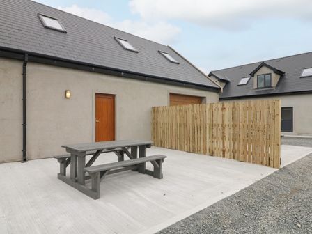 An outdoor concrete patio with a gray wooden picnic table and benches next to a building with wooden door and skylights at Old Field Hideaway Slade near Fethard-On-Sea County Wexford