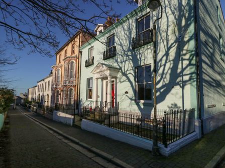 A row of multistory houses along a narrow street with trees casting shadows on the buildings at 8 Corkickle in Whitehaven