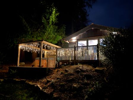 A cabin with a wooden deck and string lights at night at Sir George Baker Cabin in Uplyme