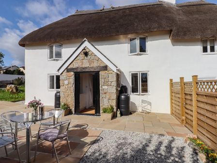 An outdoor patio area with metal table and chairs stone entrance and wooden fence at Cob Cottage in Bovey Tracey
