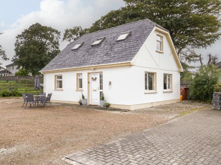 A white house with a gray roof and skylights a patio table with chairs and an umbrella in the yard at Shore Road in Culdaff County Donegal