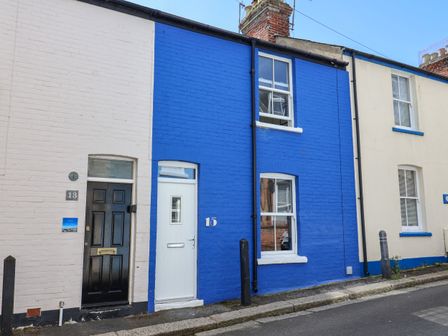 A street view of terraced houses with one painted blue and windows and doors visible at Mackerel Cottage in Weymouth