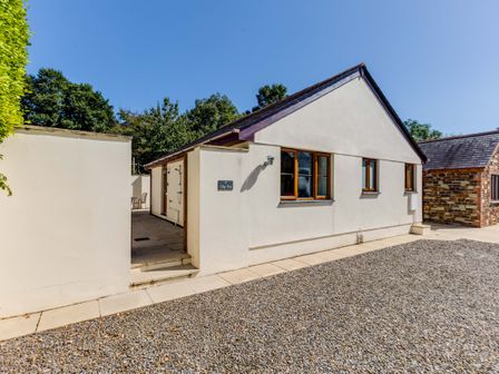 An exterior view of a single story building with white walls and brown framed windows with a gravel ground area at Chy Pol in St Minver