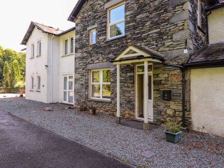 The exterior of a stone and white plaster house with a pebble driveway and a small porch at Silver How in Ambleside
