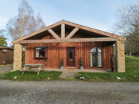 A wooden cabin with a picnic table outside and trees in the background at Matfen in Longframlington