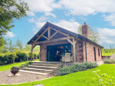 A stone cottage with wooden beams on the porch and outdoor furniture on the steps at Waters Edge in Talkin near Brampton Cumbria