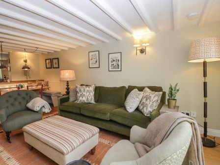 A living room with green sofa armchairs striped ottoman and dining area at Kyte Cottage in Ilmington