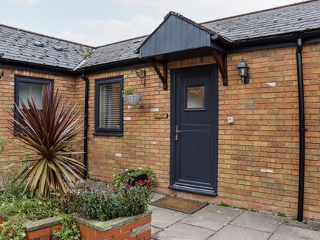 The entrance of a brick house with a dark gray door and window with plants in a garden bed at Fern Cottage in St Brides-Super-Ely