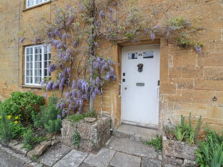 A white door with the number 23 and flowering plants growing on a stone wall at Two Towers Cottage in Montacute
