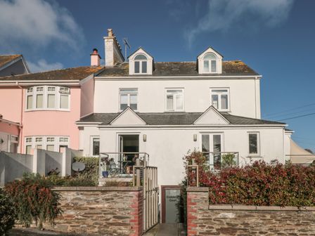 A white multi story house with chimneys small balconies and a stone wall with plants at Hamnavoe in Stoke Fleming
