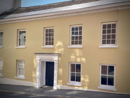 The exterior of a yellow building with white window frames and a dark blue door in Lyme Regis