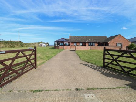 A driveway leading to a brick house with a conservatory and two wooden gates open at Beach Haven in Happisburgh East Anglia