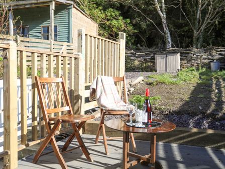 An outdoor patio with two wooden chairs and a small round table with a bottle and glasses at 4 Ty Person in Braichmelyn near Bethesda