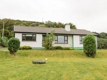 A single story house with white walls and green trim with bushes and grass in front at Drumore House Laddan near Carrigart County Donegal